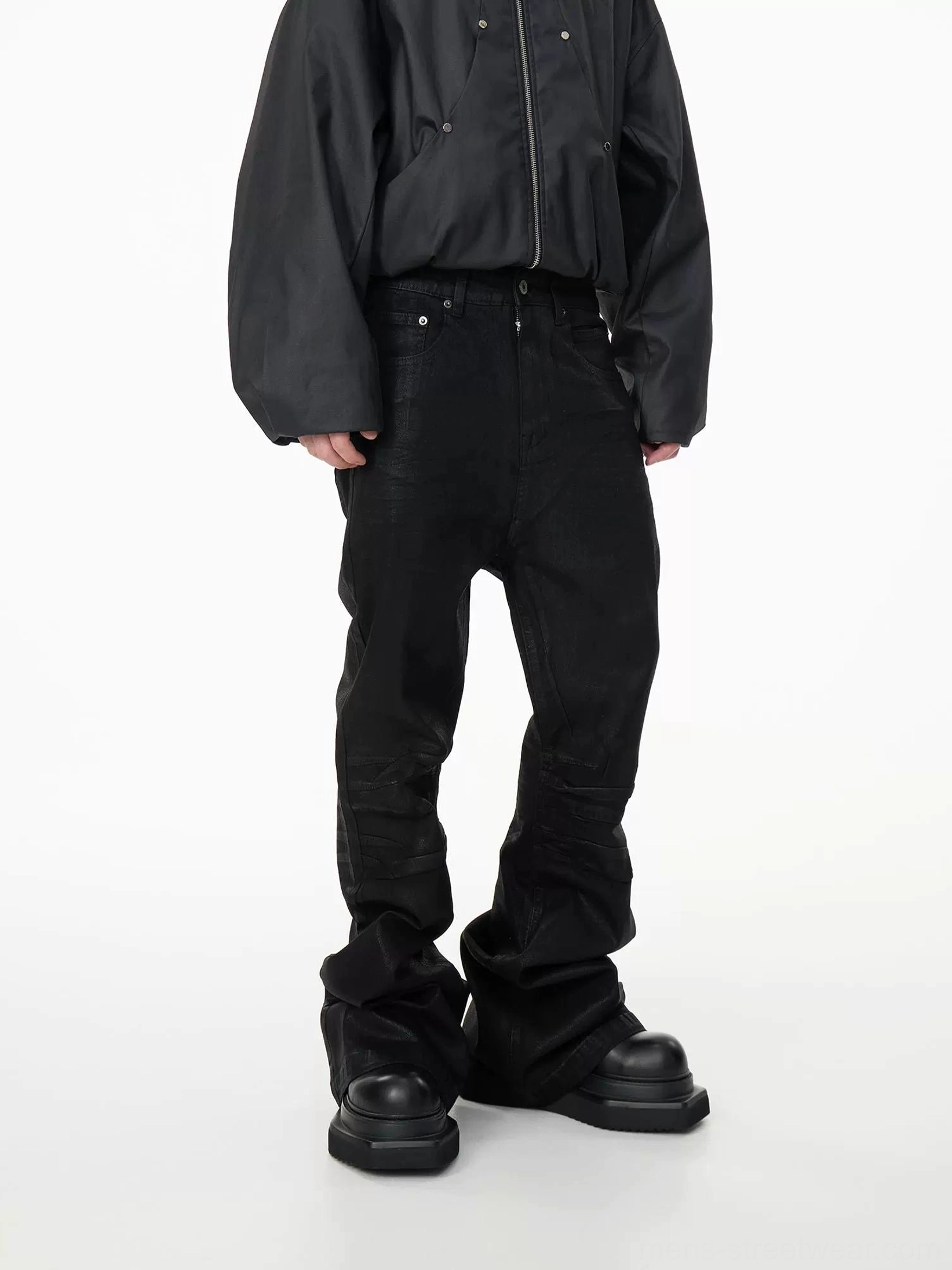 Right front three-quarter view of black stacked denim jeans showing thigh panel seams, rivets, and flared leg shape