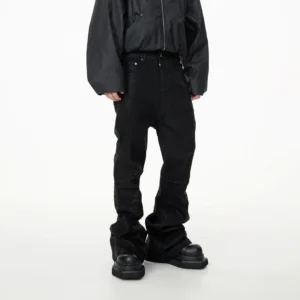 Back three-quarter view of black stacked panel denim jeans with wide flared legs and pooled hems over platform shoes