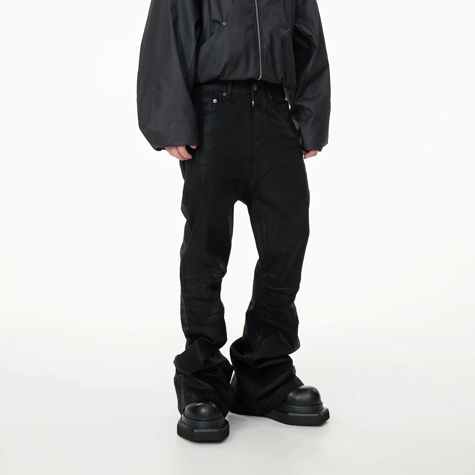 Back three-quarter view of black stacked panel denim jeans with wide flared legs and pooled hems over platform shoes