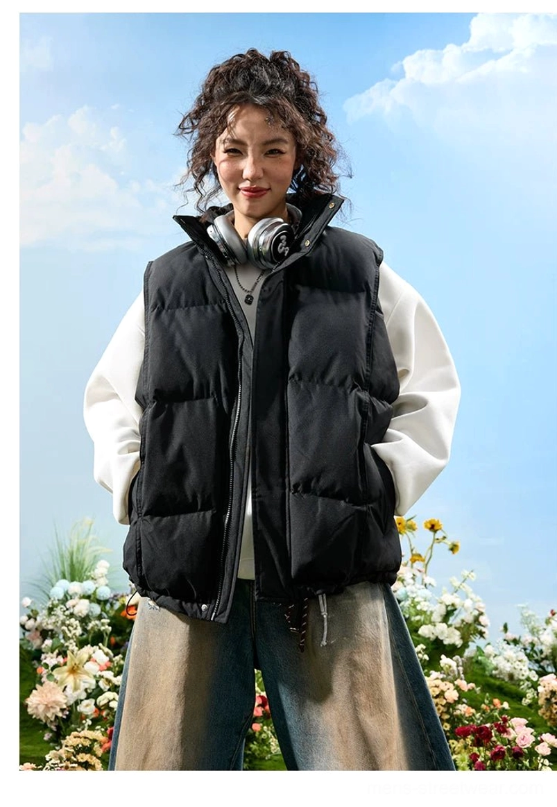 Black oversized stand collar puffer vest worn over a white sweatshirt with headphones for a casual urban streetwear look