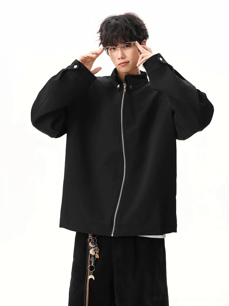 Black stand collar zip jacket fully fastened showing silver front zipper loose sleeves and clean modern streetwear silhouette
