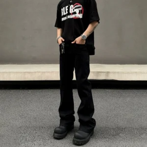 Black straight leg denim jeans front three quarter view styled with graphic t shirt and chunky black boots in an industrial streetwear setting