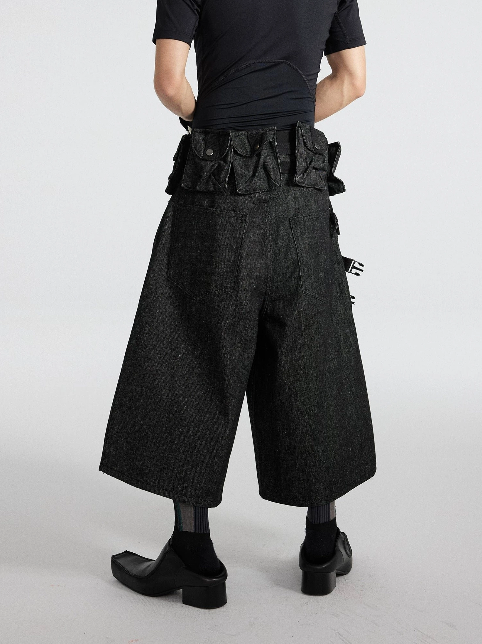 Black wide-leg tactical denim cargo cropped shorts rear angled view showing ladder straps, utility pouches, and back pockets