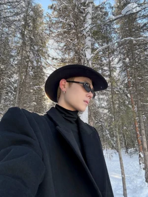 Black fitted stretch turtleneck base layer worn beneath a black wool overcoat in a snowy forest, showcasing minimalist Korean streetwear winter styling