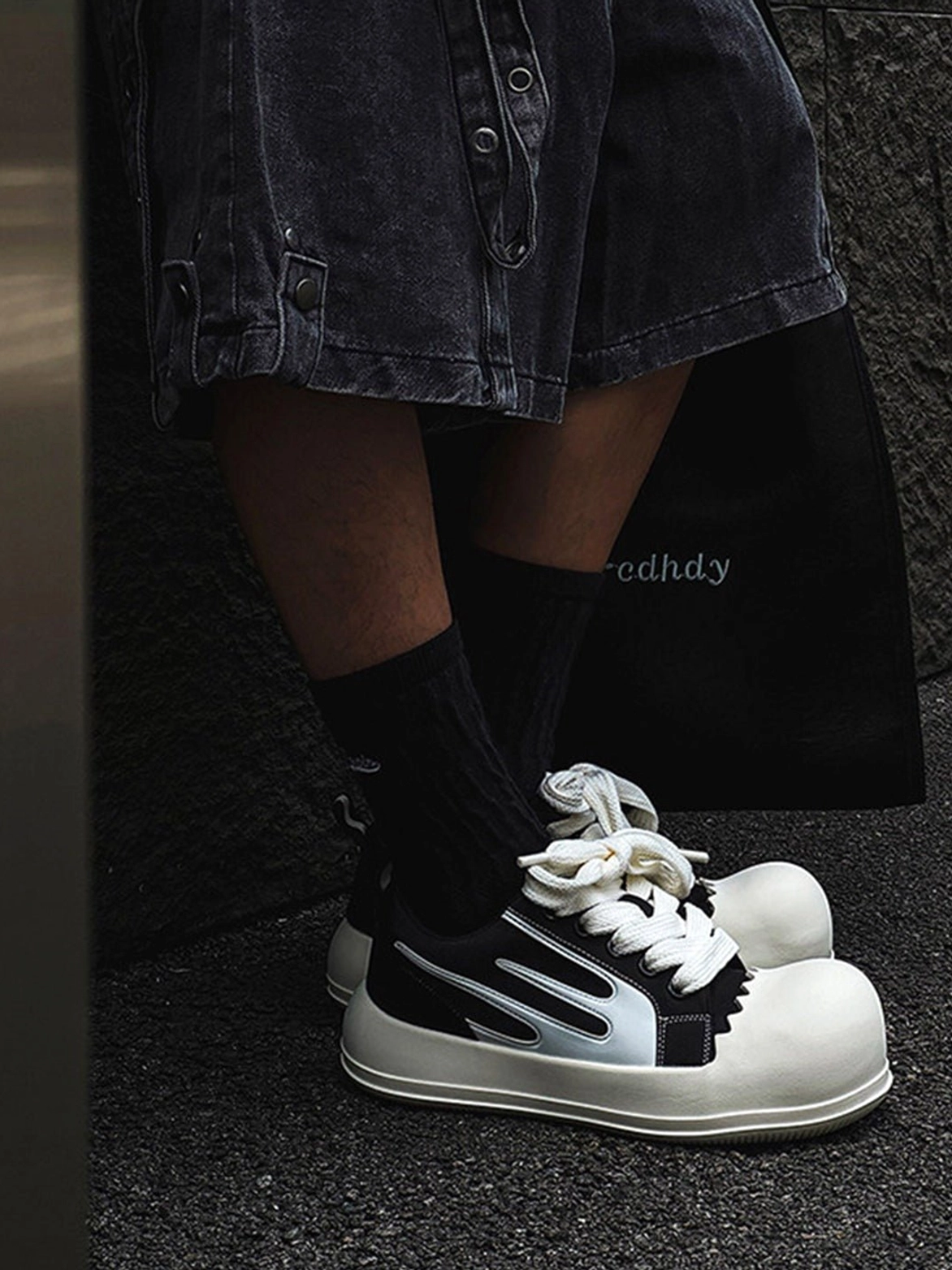 Side view of black chunky platform sneakers with silver white stripes oversized white toe caps worn for streetwear styling