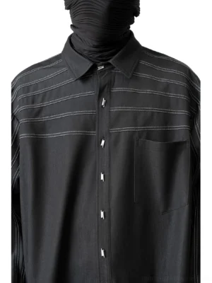 Close-up front view of black oversized streetwear shirt showing pointed collar, metal-style buttons, chest pocket, and contrast stripe stitching