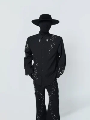 Front three-quarter view of a black studded constellation shirt with pearl-look rhinestone details, pointed collar, metal triangle collar tips, and relaxed streetwear fit styled with flared trousers