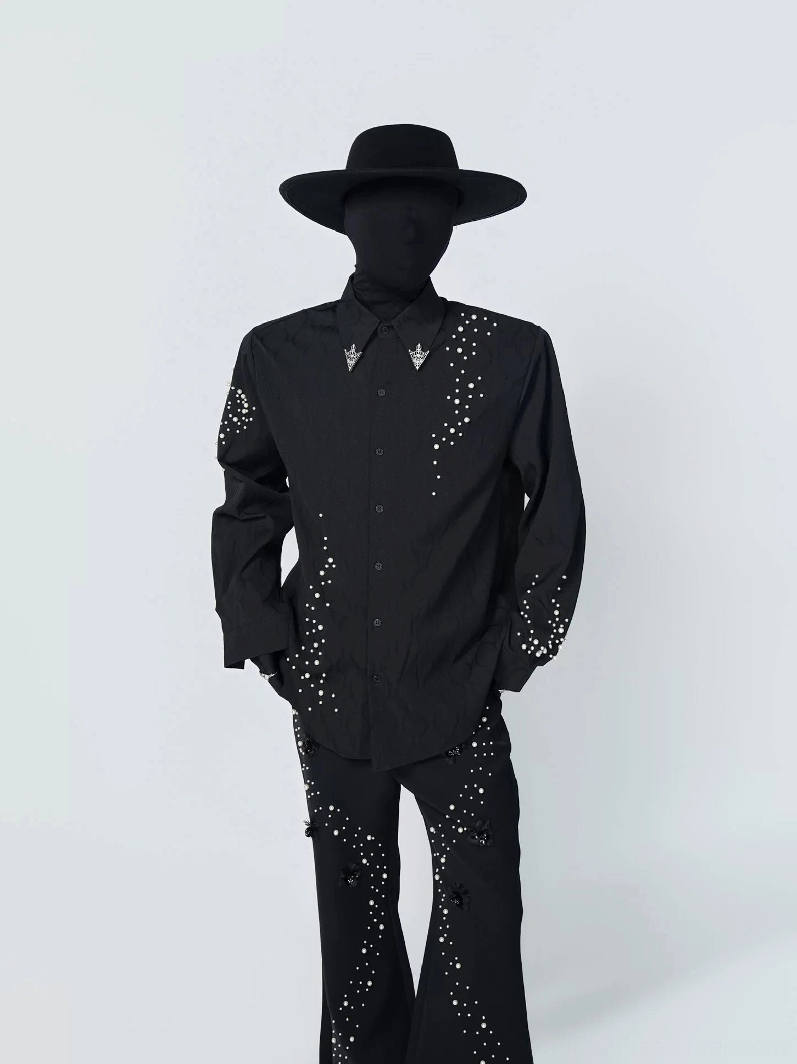 Front three-quarter view of a black studded constellation shirt with pearl-look rhinestone details, pointed collar, metal triangle collar tips, and relaxed streetwear fit styled with flared trousers