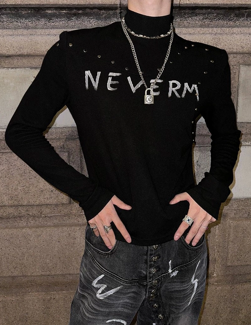 Full-body male model wearing a black studded gothic knit turtleneck with chest graphic, collar studs, printed jeans, and layered streetwear accessories