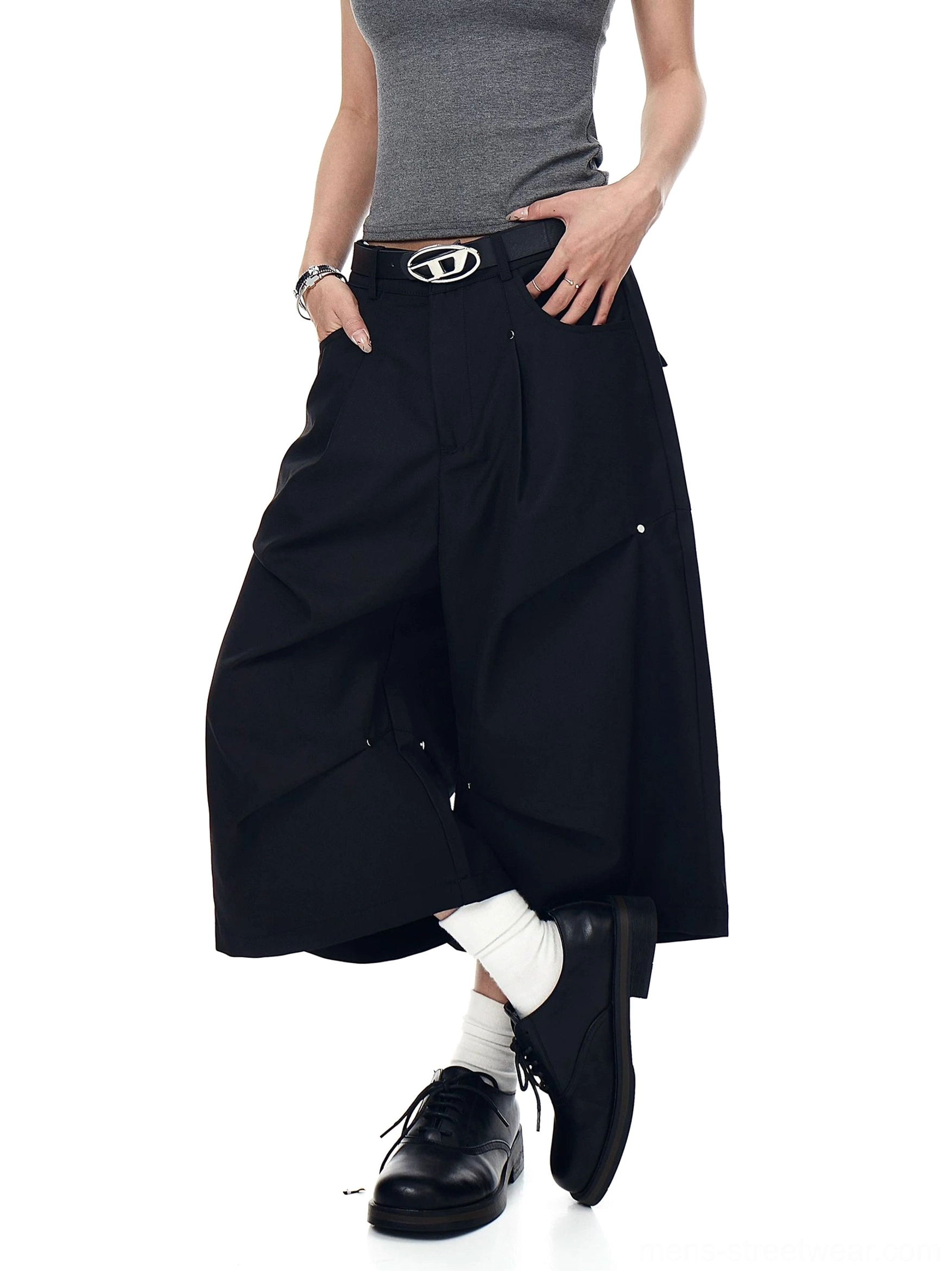 Black studded pleated longline shorts shown from a three-quarter angle with wide cropped legs and metal rivet accents