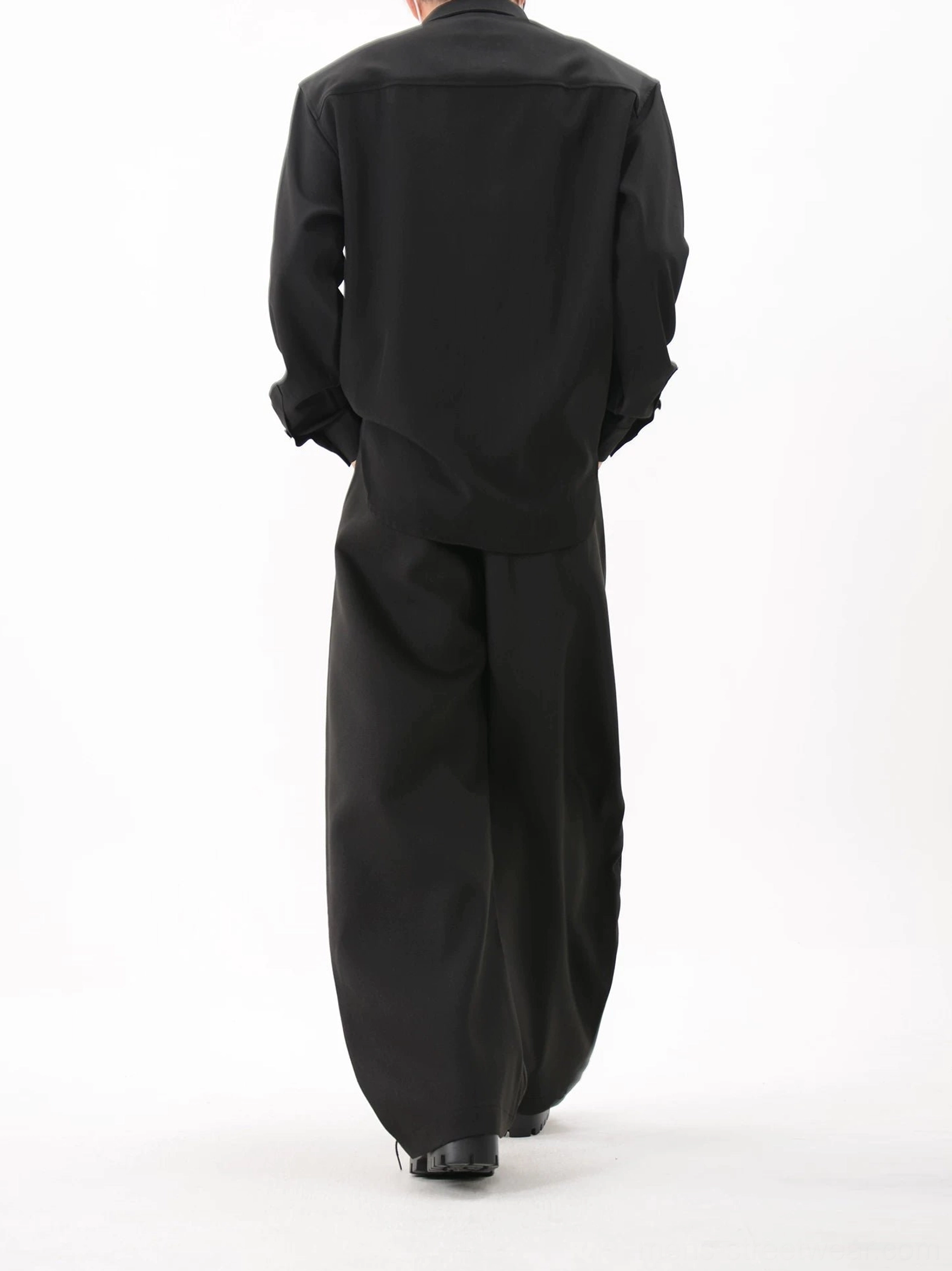 Rear view of black studded streetwear overshirt styled with black wide-leg trousers and polished shoes, showing the clean minimal back