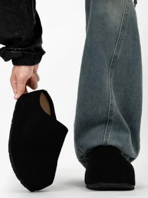 Black suede platform clogs shown from a low side angle with a closed box toe and chunky slip-on sole styled with loose blue jeans