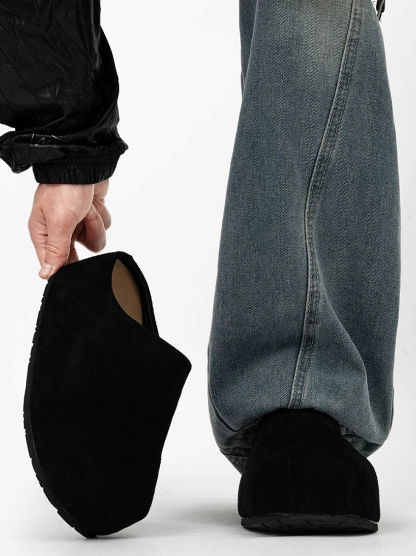 Black suede platform clogs shown from a low side angle with a closed box toe and chunky slip-on sole styled with loose blue jeans