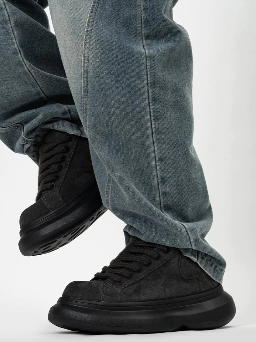 Black suede platform sneakers worn with blue wide-leg denim, featuring an all-black upper, chunky sole, and low-top lace-up silhouette