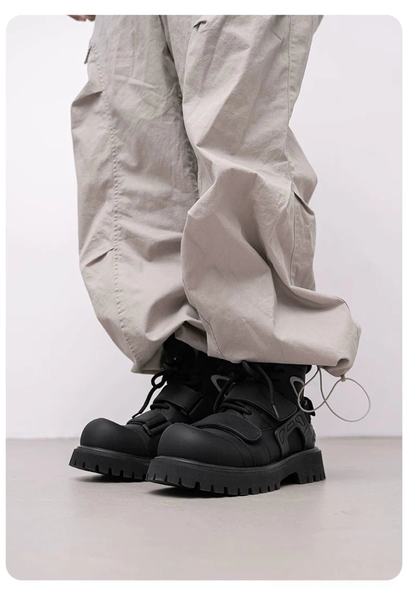 Pair of black high-top tactical harness boots worn with loose gray cargo pants, featuring rounded toes and chunky platform lug soles