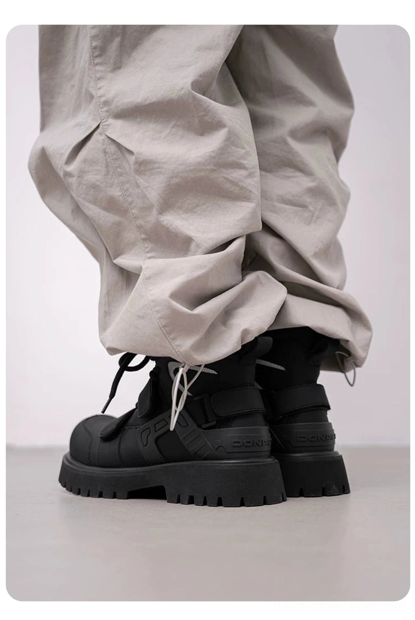 Rear view of black tactical combat boots with high shafts and thick platform outsoles styled with cuffed beige cargo trousers