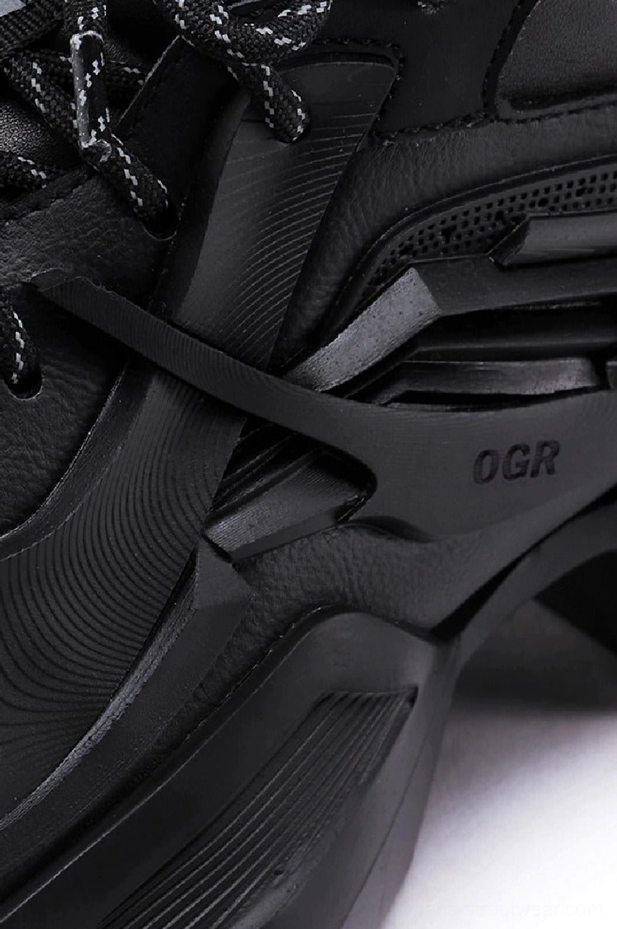 Close-up side detail of matte black tactical platform sneaker with reflective laces, structured upper panels, and chunky streetwear outsole