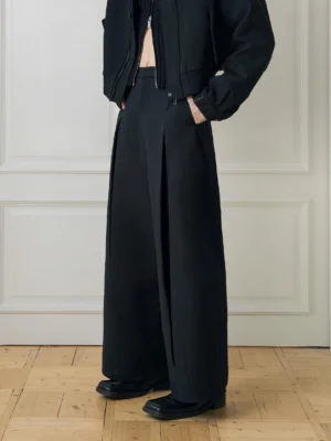 Three-quarter view of black tailored wide-leg trousers showing the button and zip waistband, structured pleats, and relaxed Korean streetwear fit