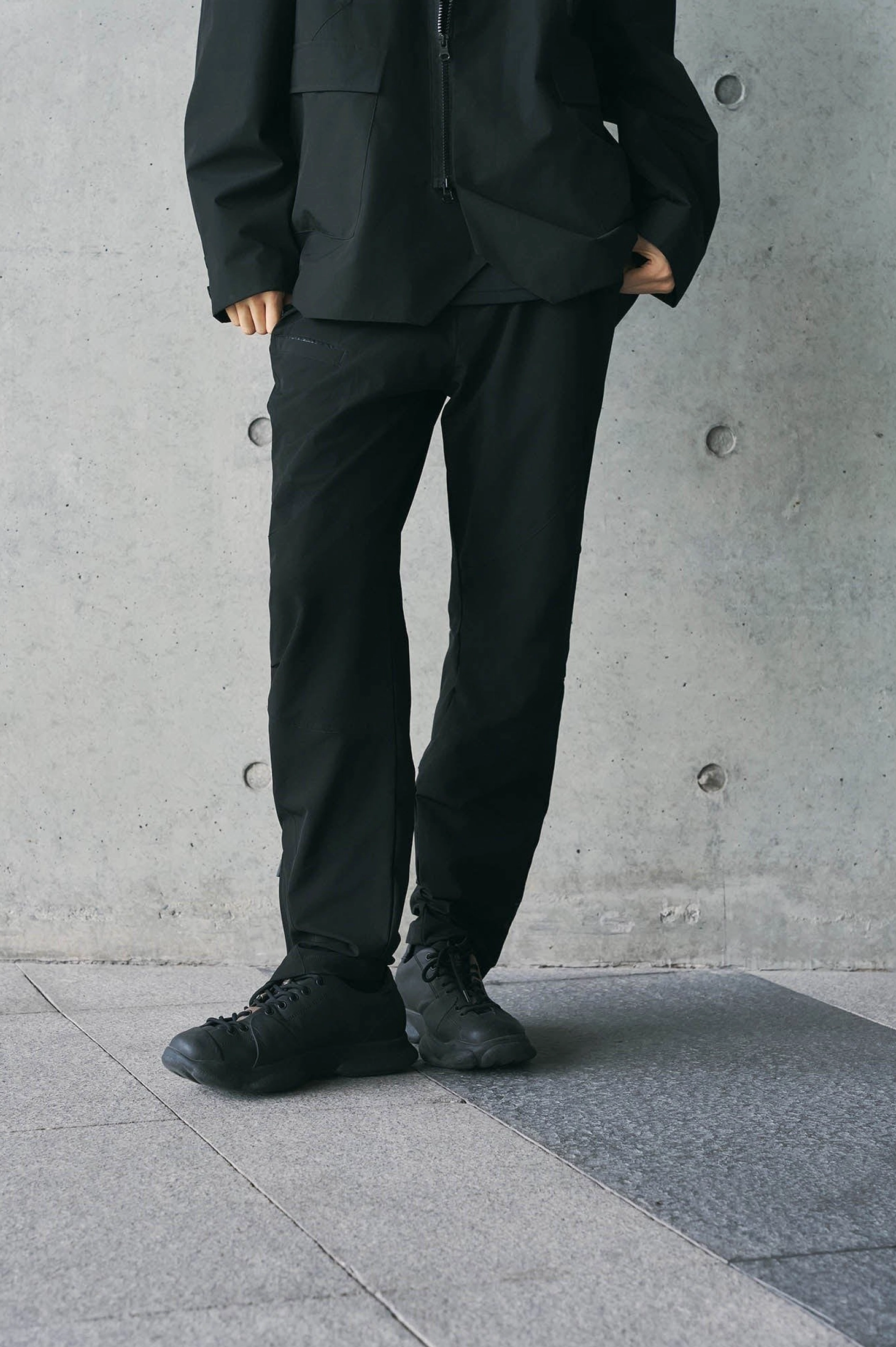 Front view of relaxed black tech crinkle track pants styled with black work boots and utility streetwear jacket