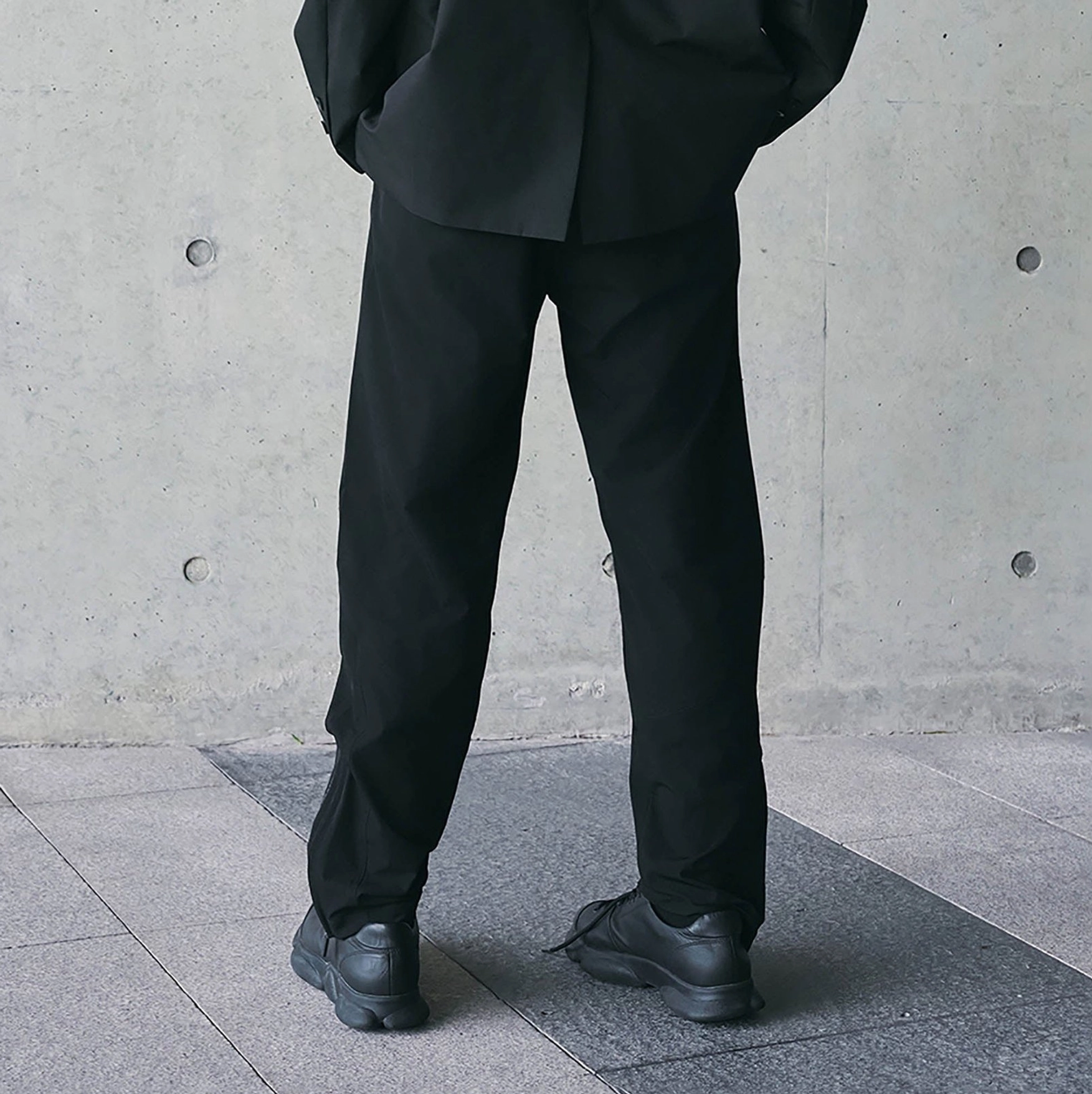 All-black technical track pants shown from the front with relaxed straight leg silhouette styled with black work boots