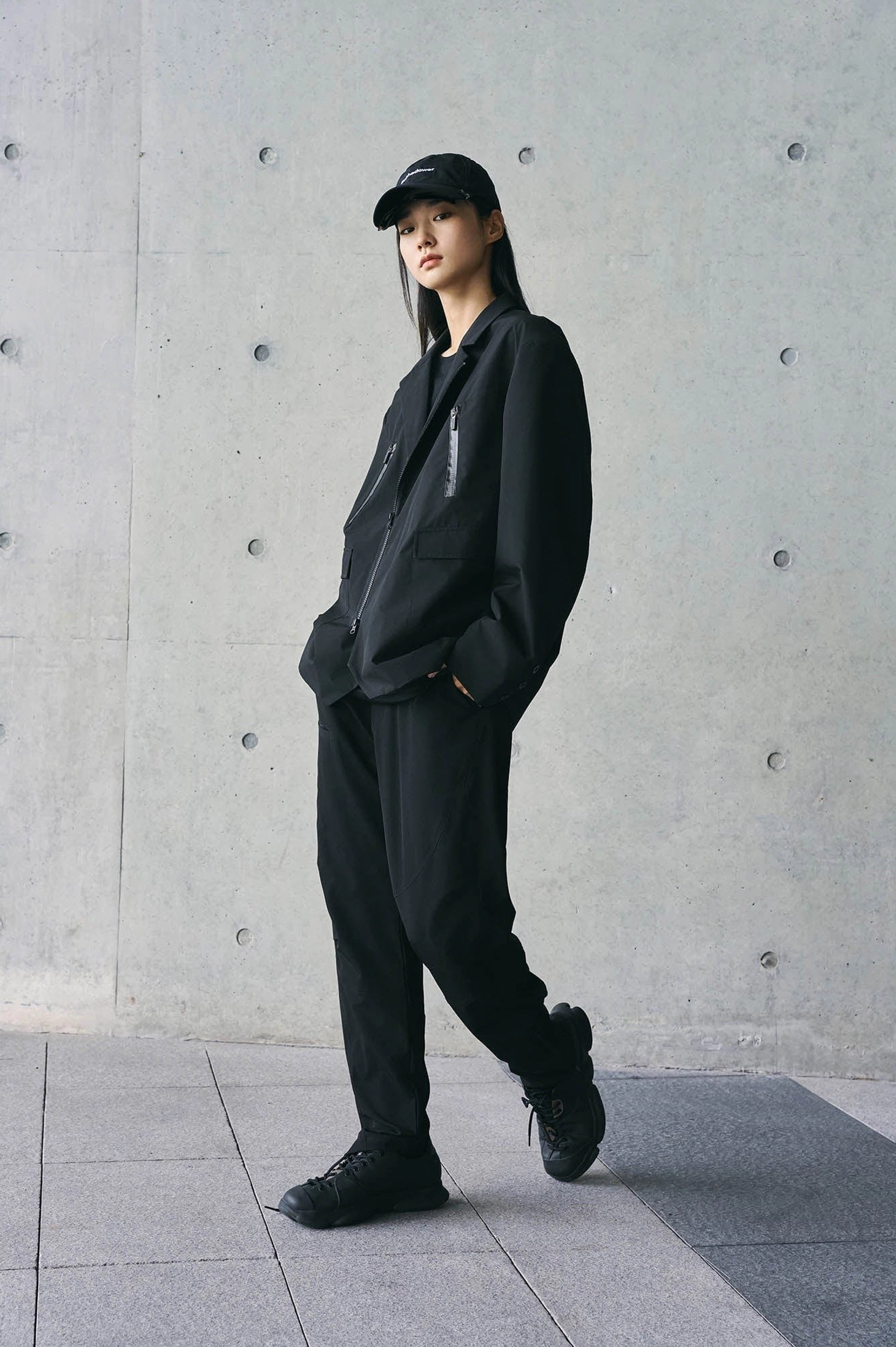Side walking view of black technical track pants and matching jacket in a minimalist urban streetwear outfit