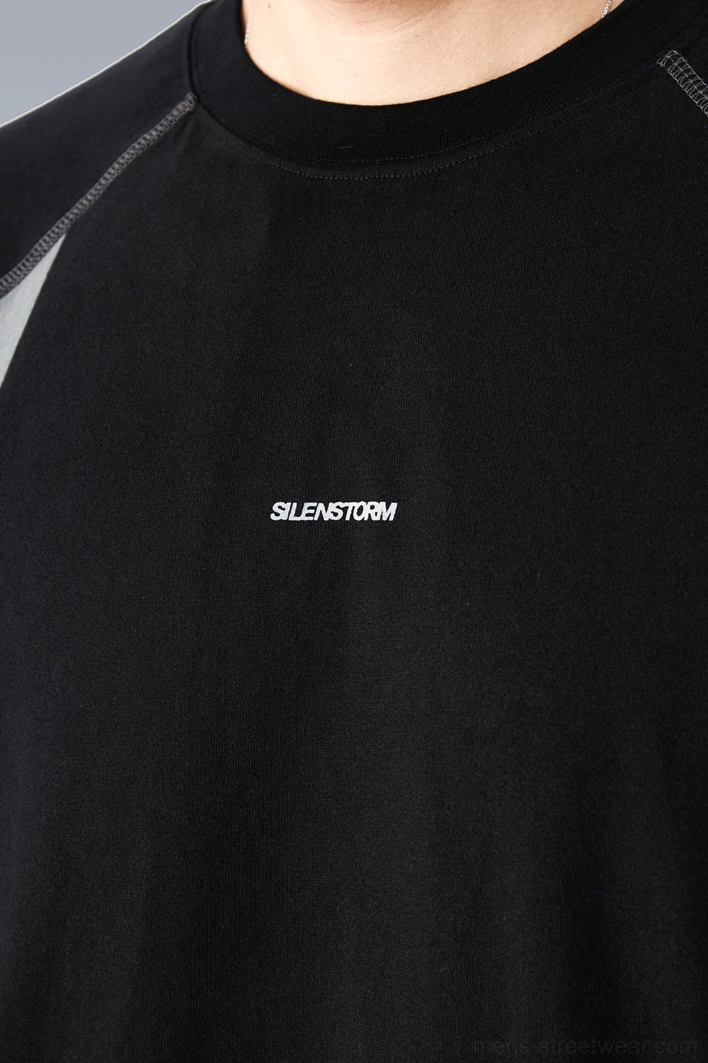 Close-up front view of a black techwear T-shirt showing the ribbed crew neck, small chest graphic, and solid cotton-style base