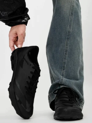 Black techwear trail sneakers shown from a rear oblique angle with a chunky anti-slip EVA outsole, matte mesh upper, and casual blue jeans streetwear styling