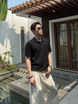 Black textured cable knit polo shirt in a relaxed fit, shown on a male model wearing sunglasses in a poolside courtyard