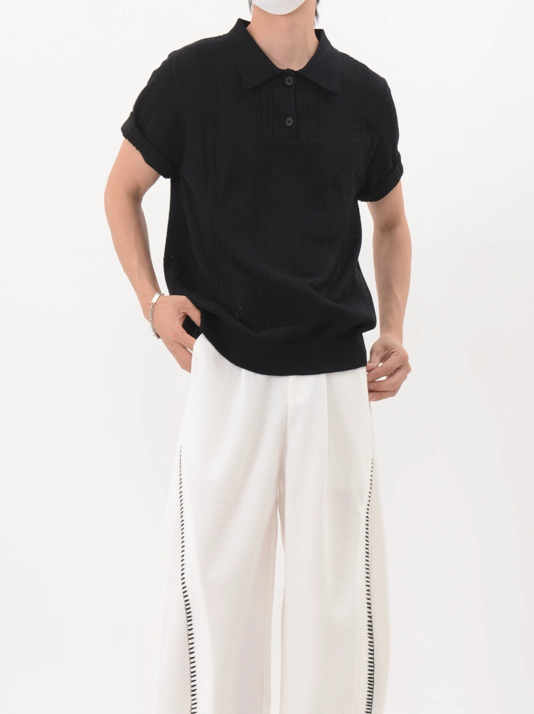 Close front view of black textured knit polo shirt showing the classic collar button placket and ribbed hem