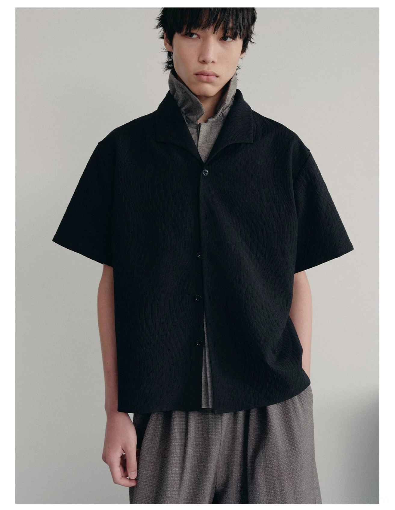 Male model wearing black textured quilted camp shirt over gray inner top with relaxed gray trousers