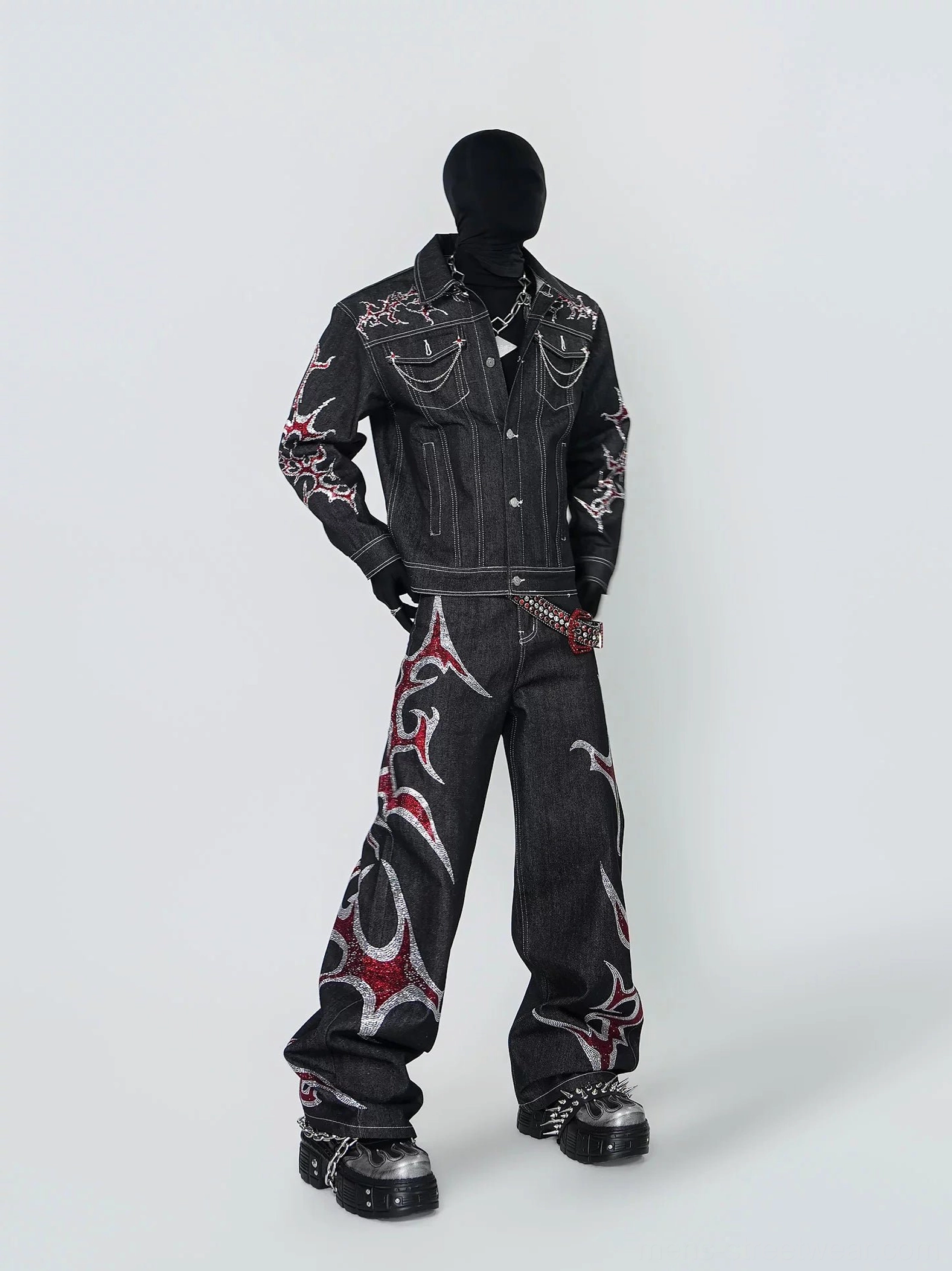 Three quarter side view of black chain trim denim trucker jacket featuring red silver tribal flame embroidery