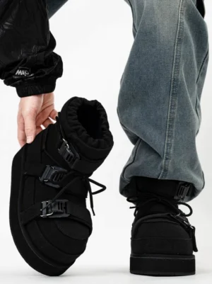Black triple-buckle quilted platform moon boots worn with blue jeans, showing padded upper, lace-up front and chunky winter sole