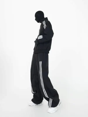 Black oversized triple stripe track suit set side view showing relaxed zip jacket wide leg pants and white sneakers