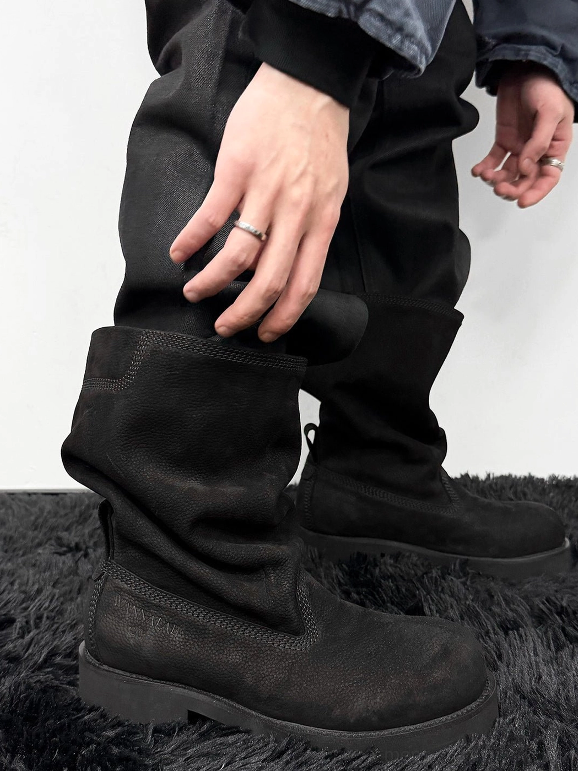 Side view of model adjusting black tumbled leather slouch mid-calf boots showing pull tab and chunky sole