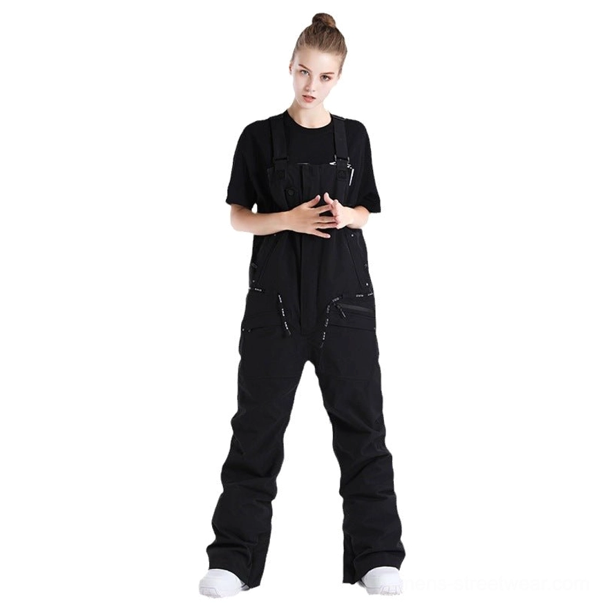Black unisex techwear bib snow pants shown in a full front studio view with adjustable shoulder buckles, relaxed straight legs, zippered cargo pockets, and insulated winter utility construction