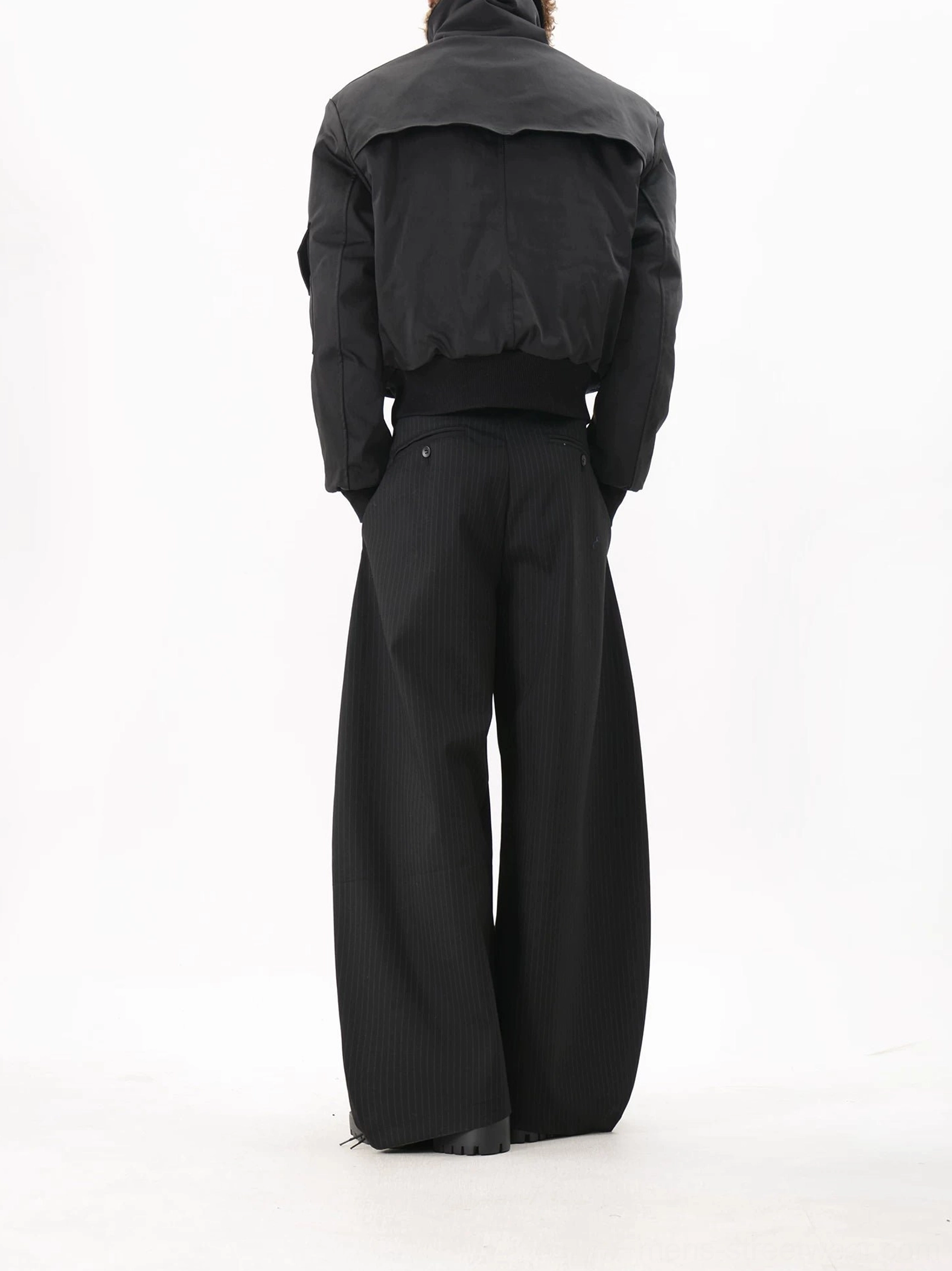 Rear view of a men's black utility bomber jacket showing the solid polyester back, structured back yoke, cropped fit and ribbed waistband