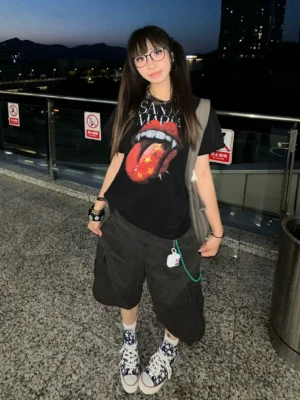 Female streetwear model wearing a black vampire lips and tongue graphic T-shirt with layered Korean fashion accessories