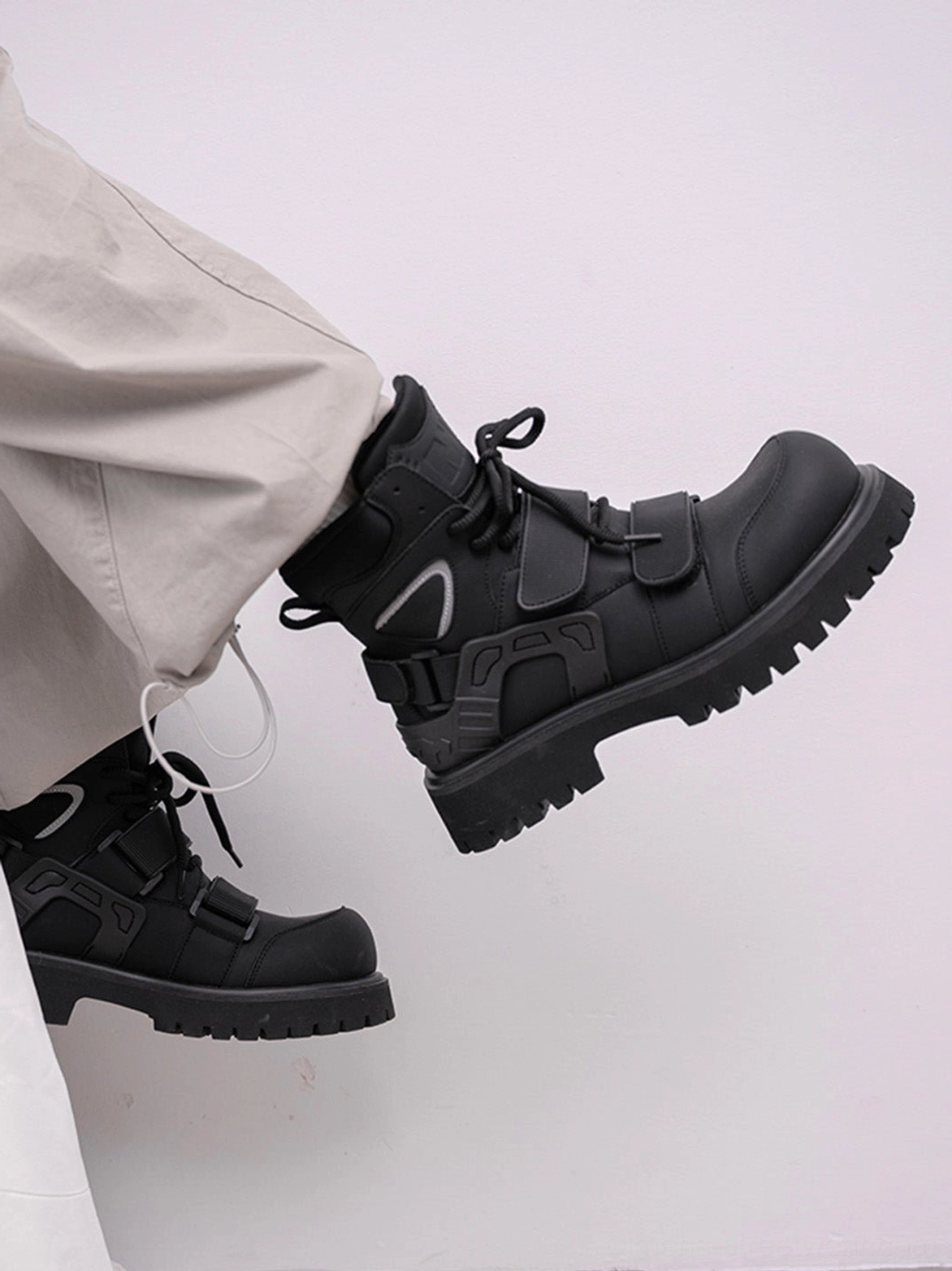 Dynamic low angle view of black Velcro strap lug sole moto combat boots showing textured outsole