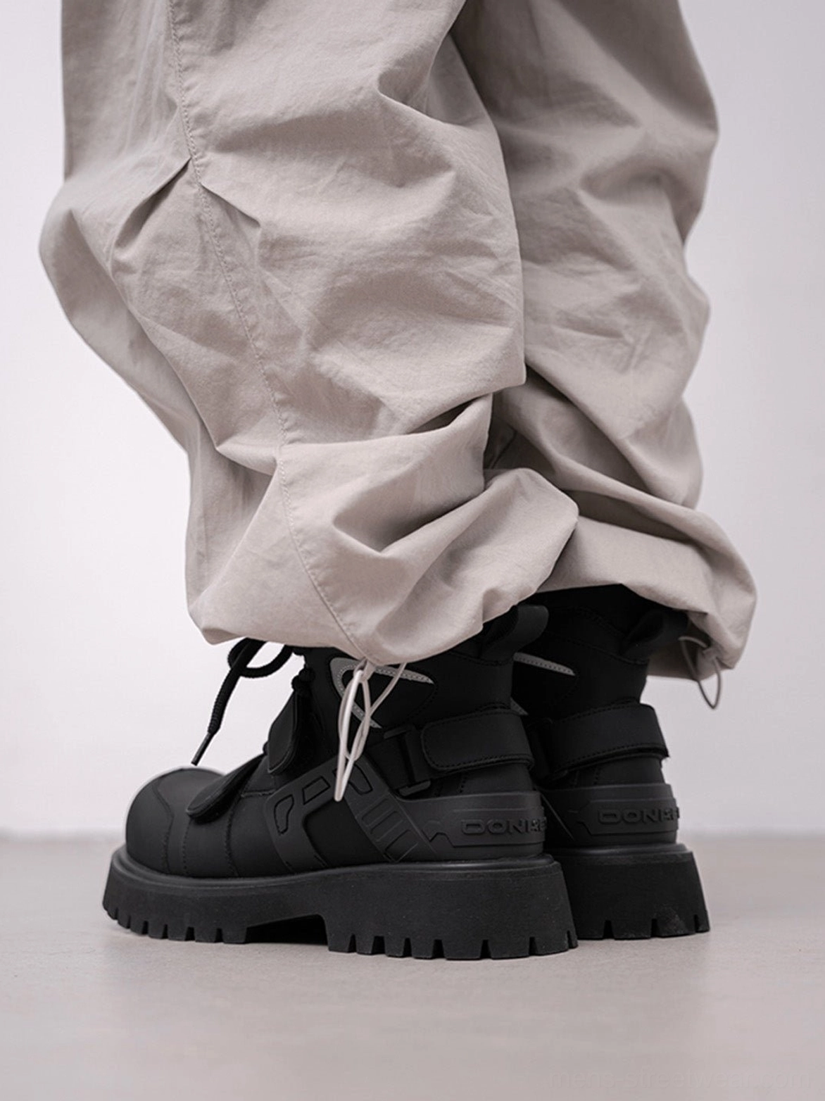 Black Velcro strap lug sole moto combat boots rear three-quarter view showing padded ankle and heel detail