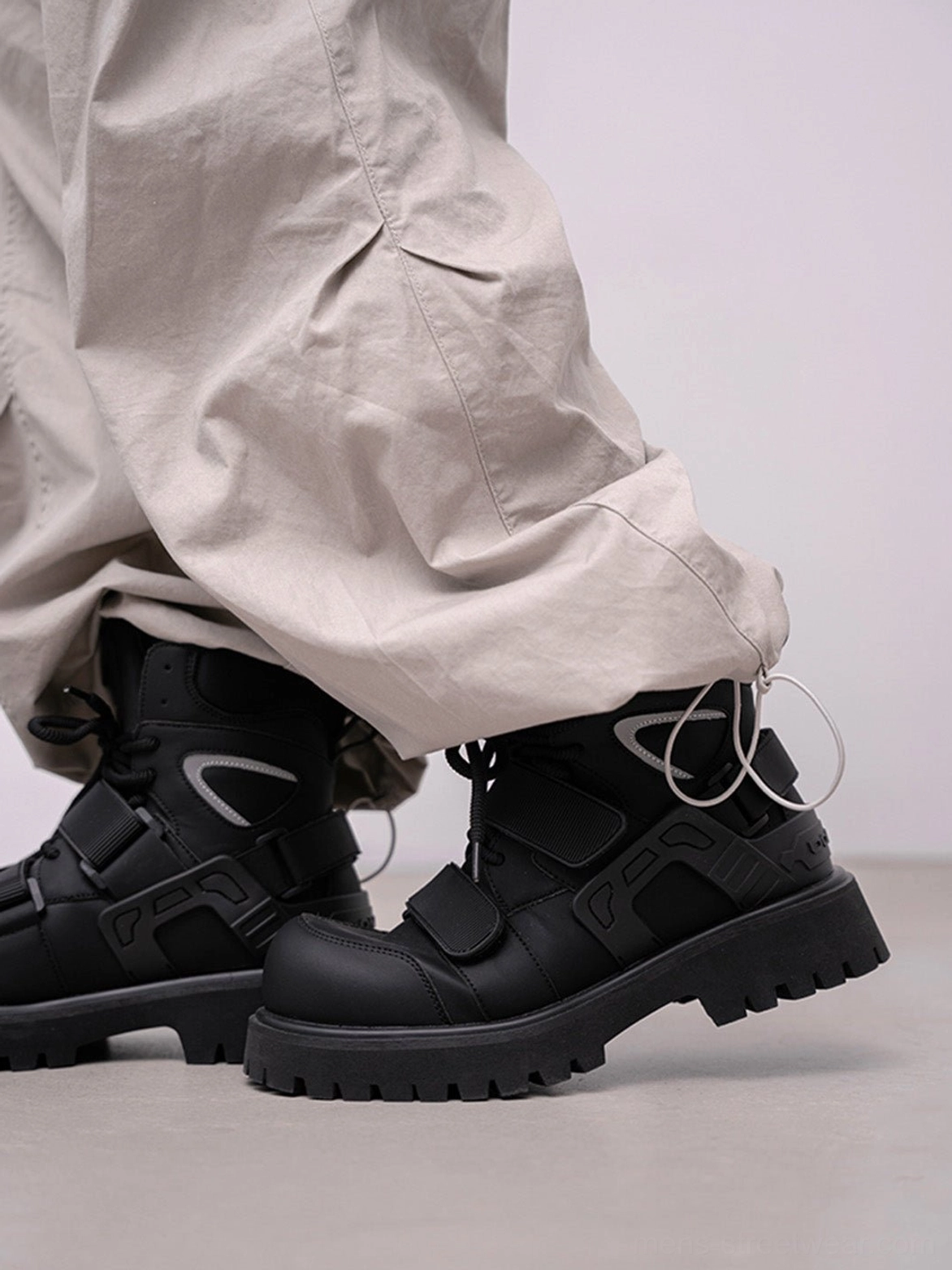 Rear view of black Velcro strap lug sole moto combat boots worn with baggy gray cargo pants