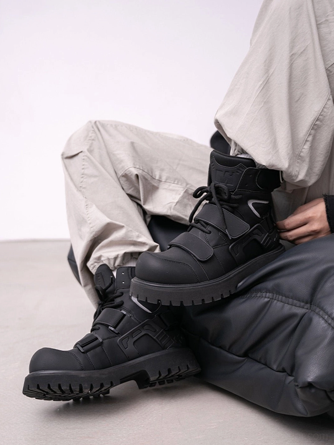 Seated streetwear styling with black Velcro strap lug sole moto combat boots and gray cargo pants