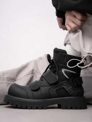 Black Velcro strap lug sole moto combat boots worn with light gray cargo pants in side profile
