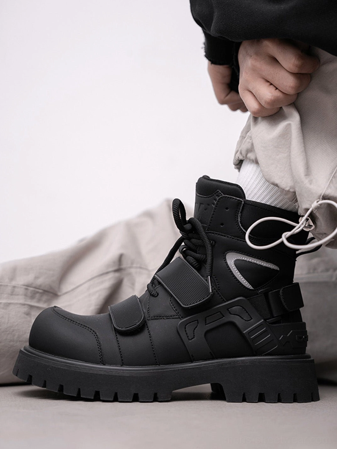 Black Velcro strap lug sole moto combat boots worn with light gray cargo pants in side profile