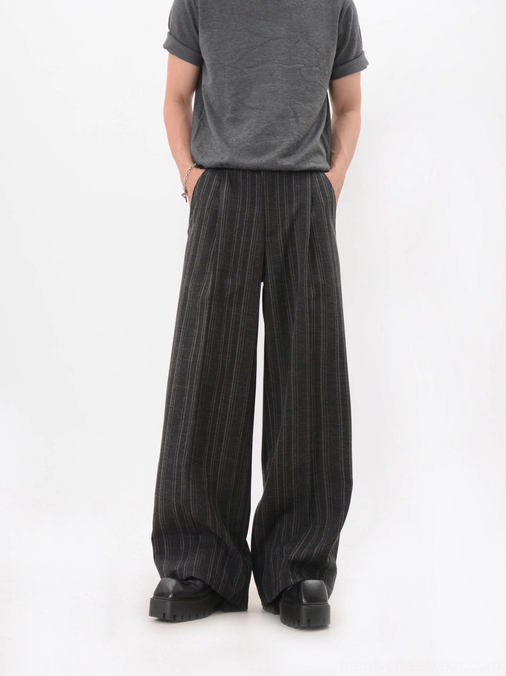 Front three-quarter view of black vertical pinstripe trousers with a loose draped leg and tailored waistband