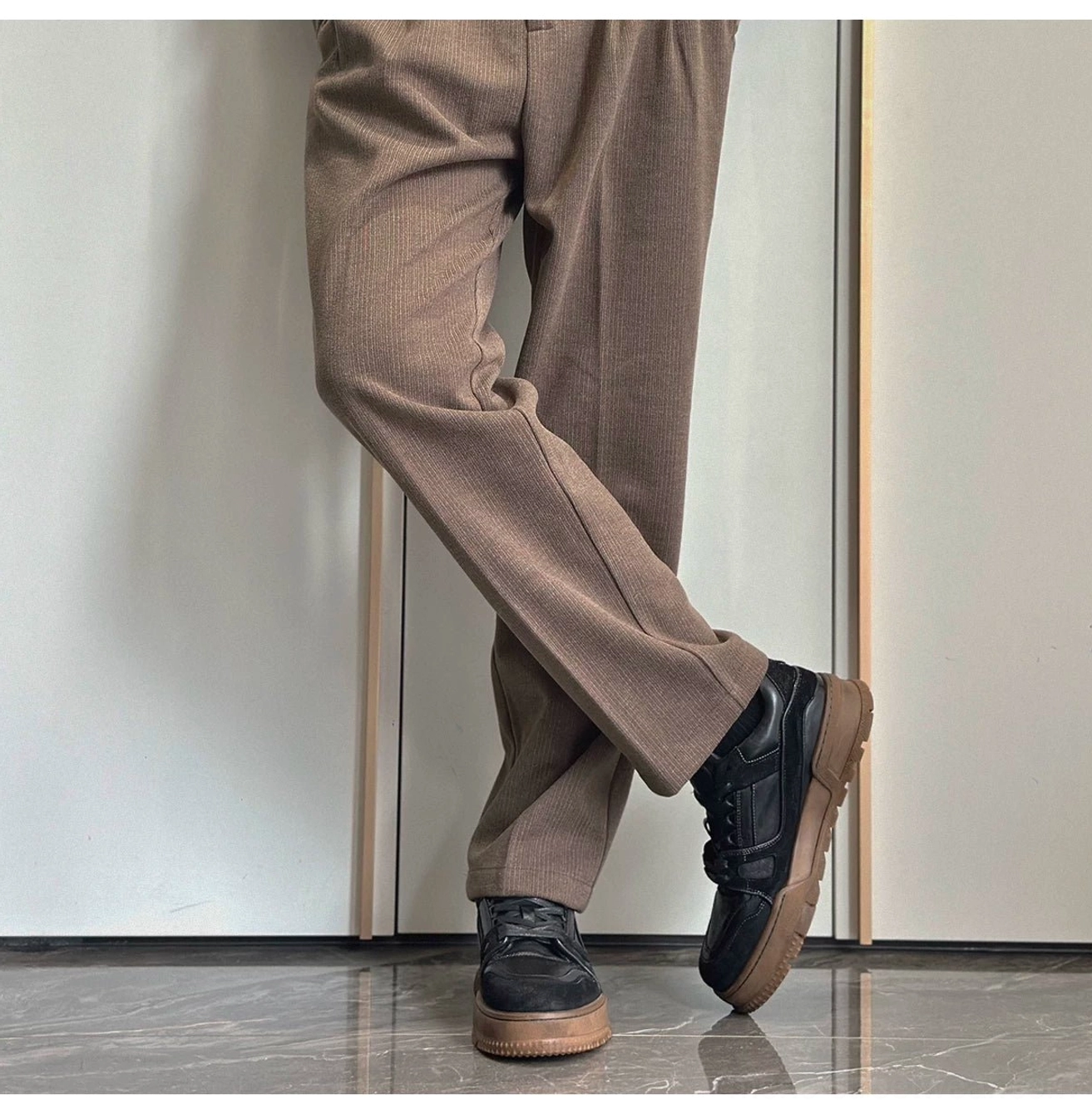 Model wearing black vintage chunky sneakers with tan tailored trousers in a minimalist indoor streetwear outfit