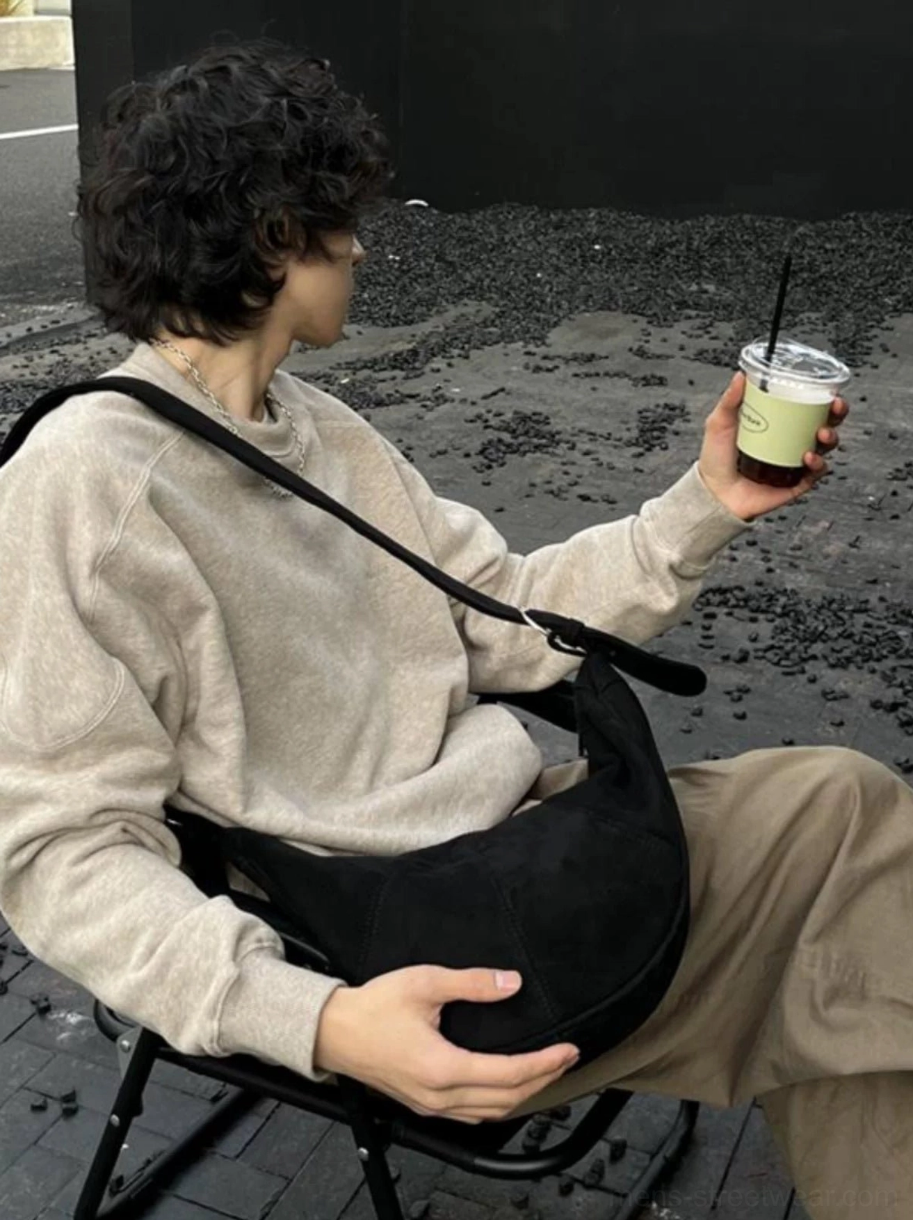 Black vintage crescent crossbody sling bag worn close to the torso while seated in a casual urban setting