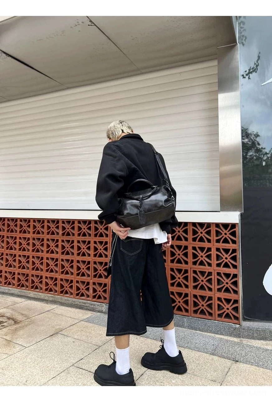 Rear full-body view of black vintage faux leather bowling bag worn crossbody with casual urban streetwear
