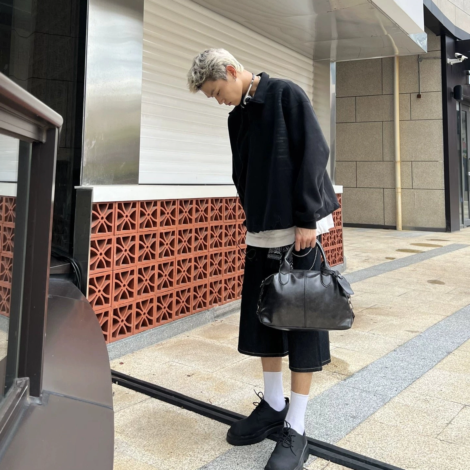 Black vintage faux leather bowling bag held by curved top handles in a modern men's streetwear setting