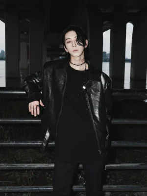 Black vintage faux leather motorcycle jacket styled with a black tee in an urban riverside setting, featuring bronze metal accents and relaxed streetwear fit
