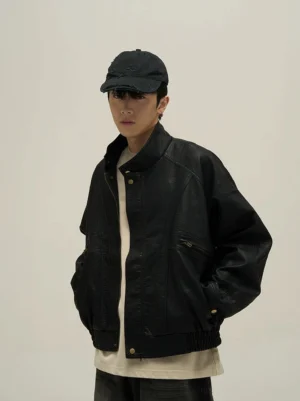 Black vintage faux leather stand collar bomber jacket front three-quarter view on male model with black cap